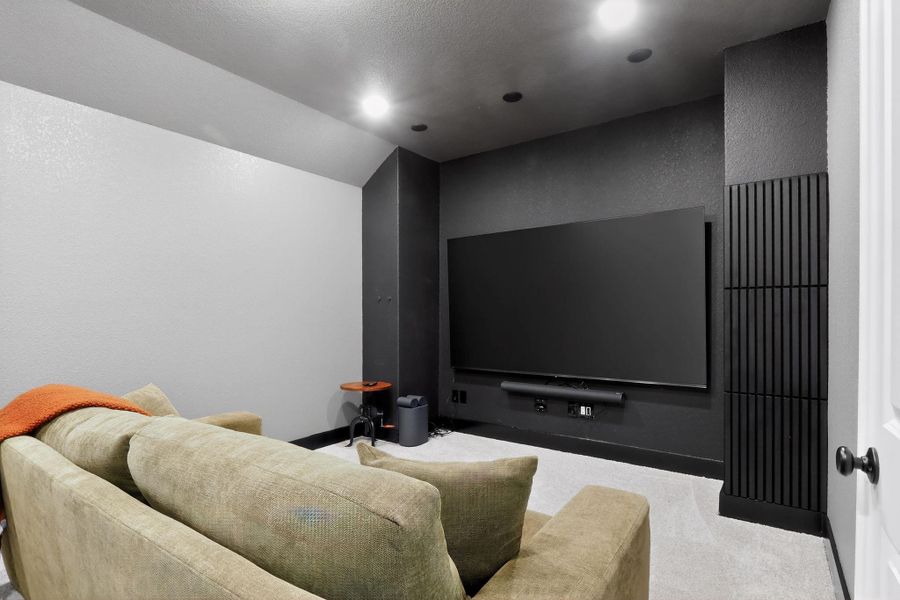 Dedicated media room featuring a large mounted screen, dark accent wall, recessed lighting, and slatted architectural detailing Dedicated media room featuring a large mounted screen, dark accent wall, recessed lighting, and slatted architectural detailing