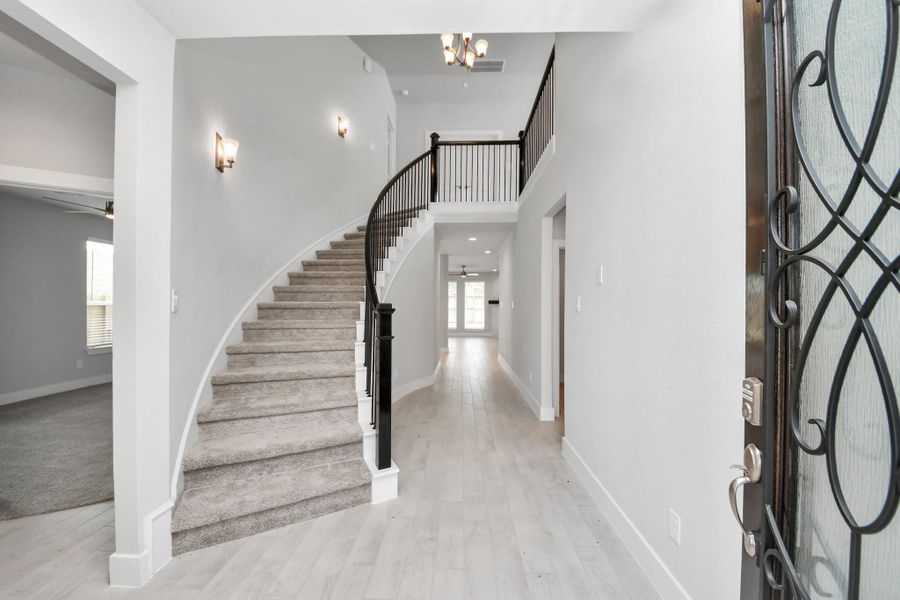 The majestic entryway allures with its high ceilings, embellished with sophisticated wood-look tile flooring and sleek oversized baseboards. Lift your eyes to a captivating sight of the open staircase, and follow the trail of natural light pouring in through expansive windows as you journey to the family room, crafting an inviting and cozy ambiance. Sample photo of completed home with similar floor plan. Actual colors and selections may vary. The majestic entryway allures with its high ceilings, embellished with sophisticated wood-look tile flooring and sleek oversized baseboards. Lift your eyes to a captivating sight of the open staircase, and follow the trail of natural light pouring in through expansive windows as you journey to the family room, crafting an inviting and cozy ambiance. Sample photo of completed home with similar floor plan. Actual colors and selections may vary.