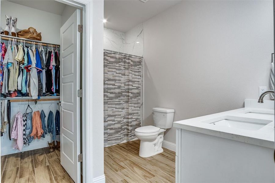Full bathroom featuring double vanity, a shower with curtain, light wood-type flooring, and a spacious closet