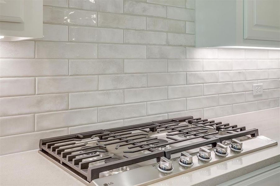 Room details with tasteful backsplash, white cabinetry, and stainless steel gas cooktop