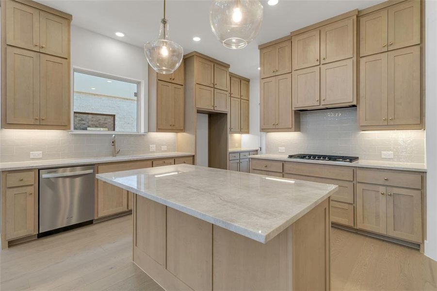 Kitchen featuring a central island with a light-toned countertop, stainless steel dishwasher, gas cooktop, light wood cabinetry, and pendant lighting