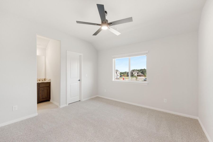 Bedroom with carpet, ceiling fan, vaulted ceiling, and attached bathroom visible through doorway Bedroom with carpet, ceiling fan, vaulted ceiling, and attached bathroom visible through doorway