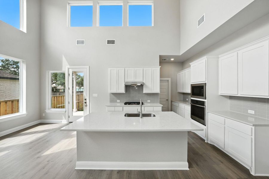 Kitchen featuring a center island with sink, dark wood-style floors, light stone countertops, white cabinetry, and decorative backsplash Kitchen featuring a center island with sink, dark wood-style floors, light stone countertops, white cabinetry, and decorative backsplash