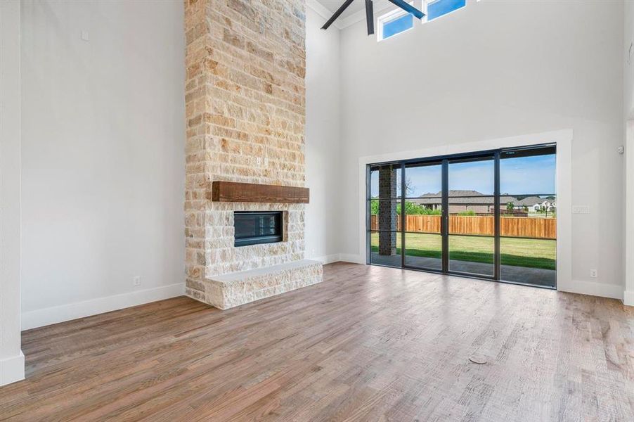 Unfurnished living room featuring hardwood / wood-style flooring, a healthy amount of sunlight, a stone fireplace, and a towering ceiling