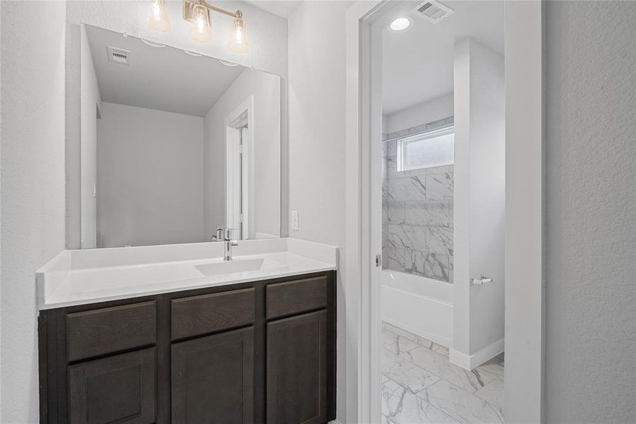 This private vanity features stained wood cabinets, beautiful light countertops, mirror, dark, sleek fixtures and modern finishes. Additionally, the shared secondary bath features tile flooring, bath/shower combo with tile surround.