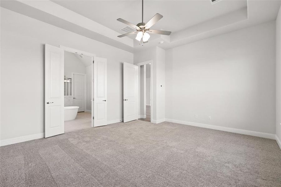 Unfurnished bedroom featuring a raised ceiling, light carpet, ceiling fan, and ensuite bath