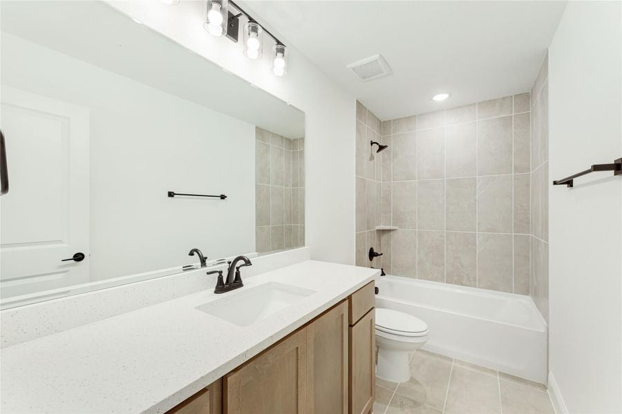 Bathroom with quartz countertop vanity, tub-shower combo with tile surround, and black fixtures