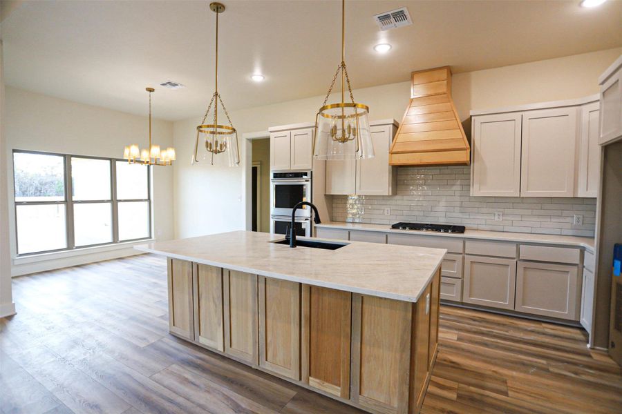 Kitchen featuring suspended lighting, a kitchen island with sink, dark wood finished floors, and two tone cabinetry