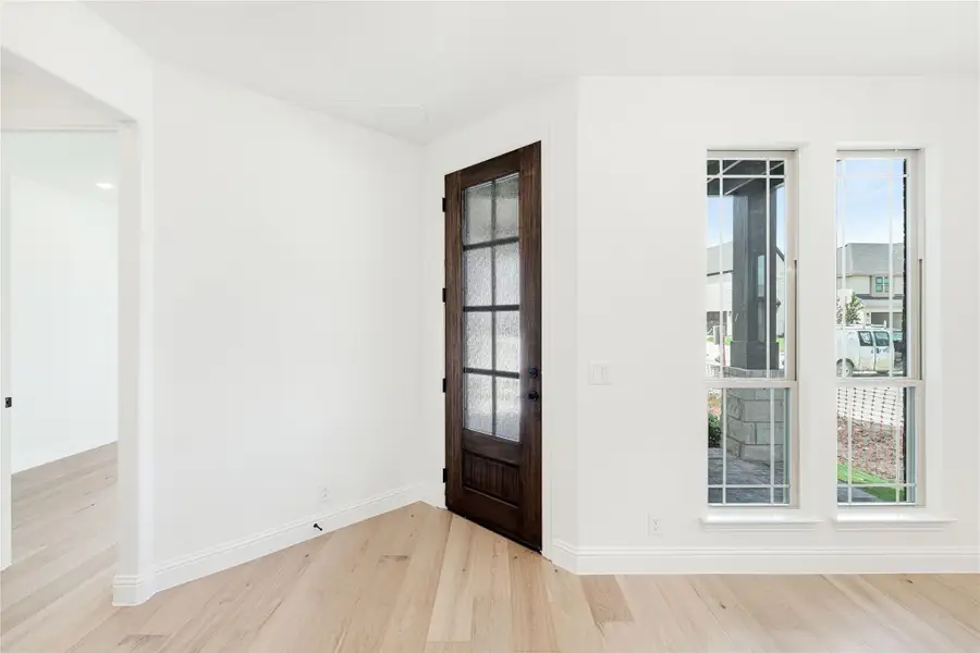 Entryway with dark wood glass-panel door, white walls, and light hardwood floors