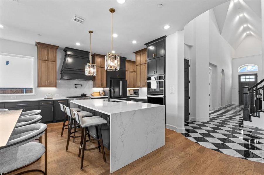 Kitchen featuring light wood finished floors, a breakfast bar, light stone counters, an island with sink, and pendant lighting Kitchen featuring light wood finished floors, a breakfast bar, light stone counters, an island with sink, and pendant lighting
