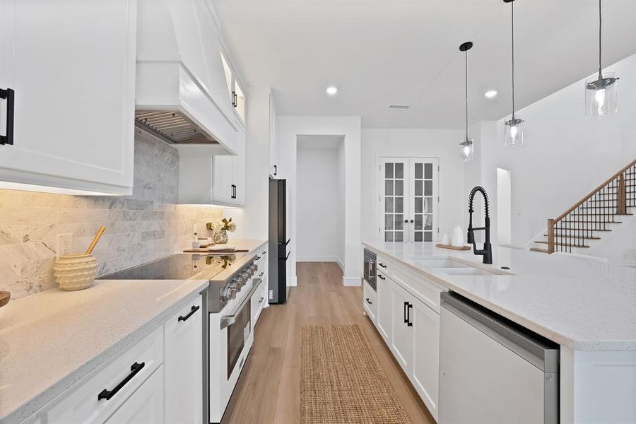 Modern kitchen featuring an expansive island with a built-in sink and black gooseneck faucet, white shaker cabinetry with matte black hardware, integrated stainless steel appliances, and wood-finish flooring