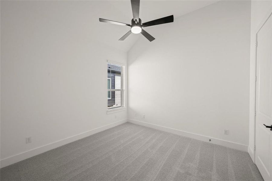 Carpeted empty room with lofted ceiling and a ceiling fan