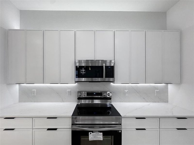Kitchen with appliances with stainless steel finishes, light stone counters, and white cabinets