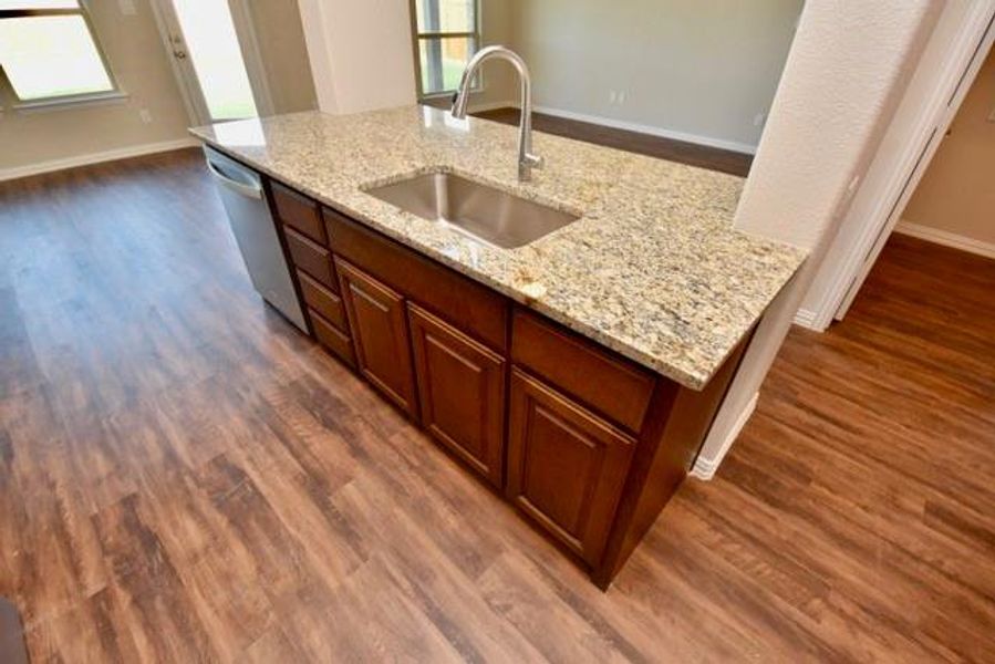 Kitchen with dark wood-style floors, light stone counters, stainless steel dishwasher, and brown cabinets Kitchen with dark wood-style floors, light stone counters, stainless steel dishwasher, and brown cabinets