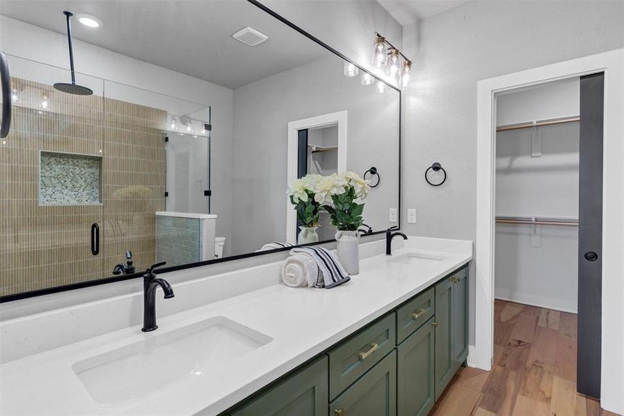 Full bath featuring a spacious closet, double vanity, a shower stall, and light wood-style flooring