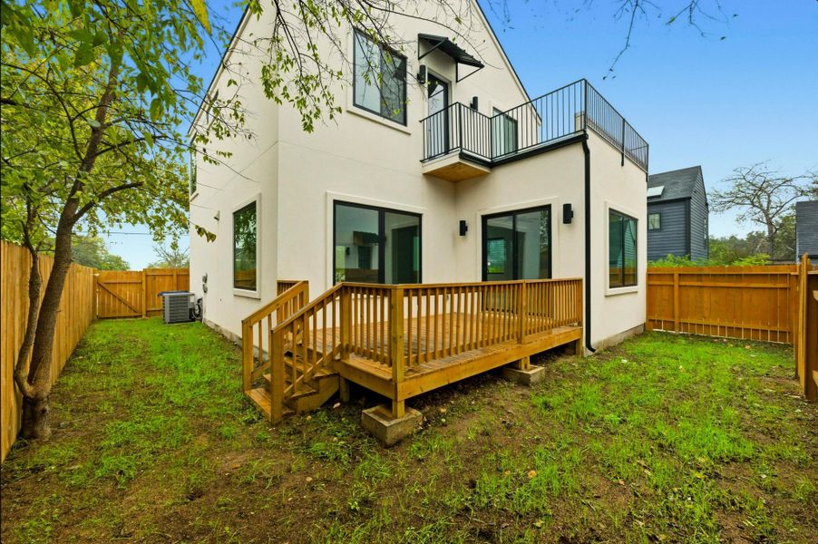 Back of property featuring a fenced backyard, stucco siding, a wooden deck, and a balcony
