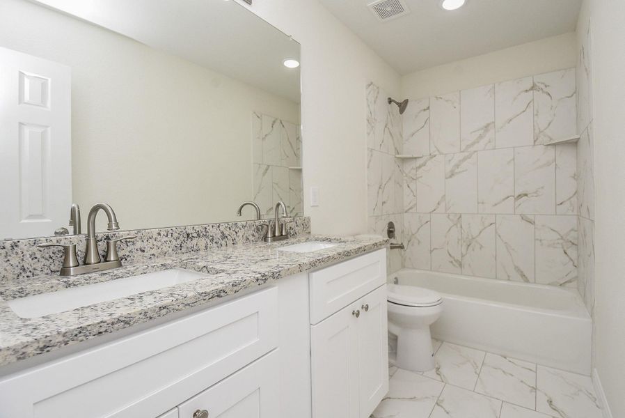 Modern bathroom with white cabinetry, granite countertops, dual sinks, large mirror, bathtub with marbled tile surround, and neutral color scheme. Modern bathroom with white cabinetry, granite countertops, dual sinks, large mirror, bathtub with marbled tile surround, and neutral color scheme.