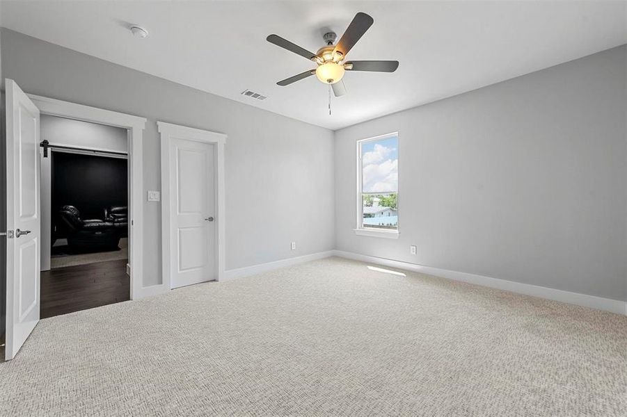 Unfurnished bedroom featuring a barn door, carpet flooring, a closet, and ceiling fan