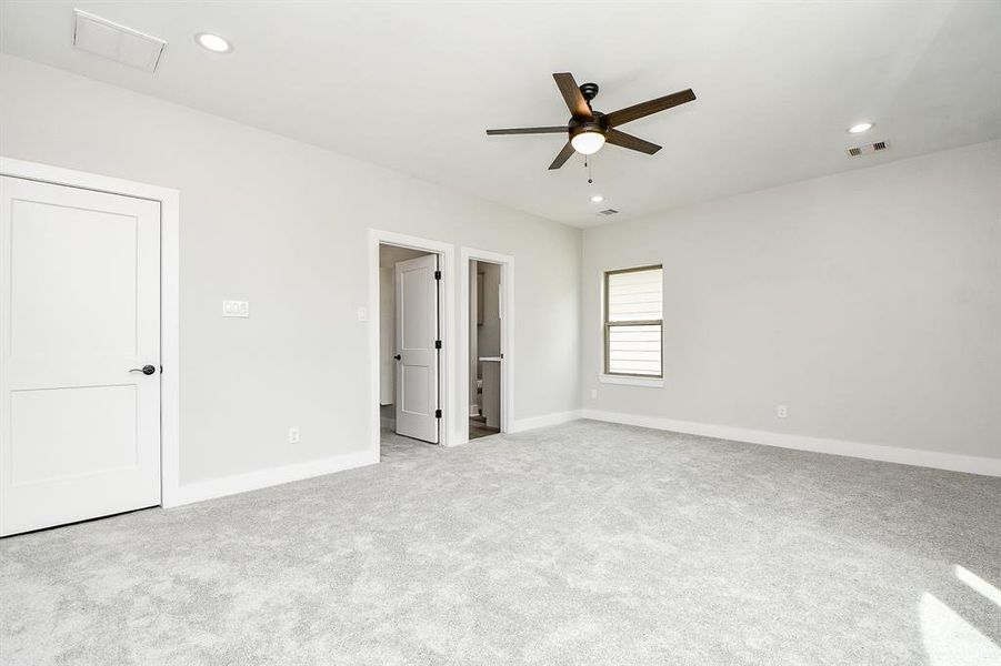 This is a spacious, well-lit room Master ensuite featuring neutral walls, plush carpeting, a modern ceiling fan with a light, and multiple doors indicating an en suite  walk in closet or bathroom. It has recessed lighting and a window for natural light.