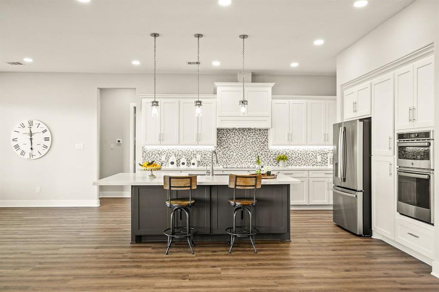 The Kitchen Island boasts closed storage on both sides, a dual basin, undermount, stainless steel sink, pull-down faucet, and trio of pendant lights. The crisp white quartz countertop has matching gray veining and overhangs on two sides, providing the perfect place for stools.