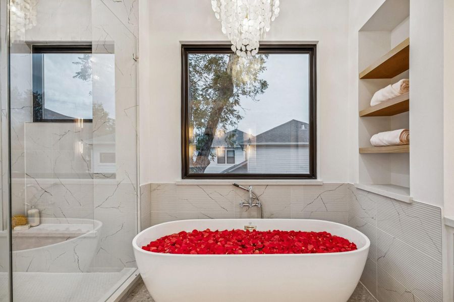 71 Inch Soaking Tub with a Wall Mounted Tub Filler, Ribbed Marble Tile Tub Surround, GlossyBronze Tiered Chandelier with Natural White Shell, White Oak Floating Shelves with a Natural Stain.