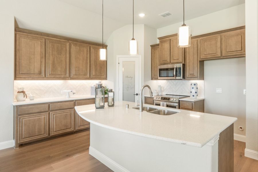 Kitchen with tan wood cabinets, white quartz island with sink, pendant lights, and stainless steel appliances