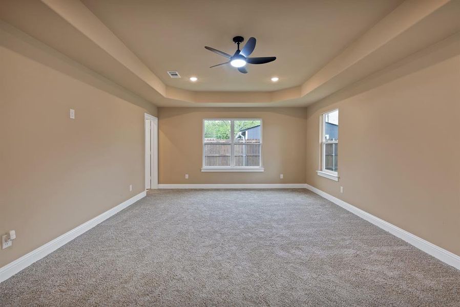 Carpeted empty room with baseboards, visible vents, a raised ceiling, and ceiling fan Carpeted empty room with baseboards, visible vents, a raised ceiling, and ceiling fan