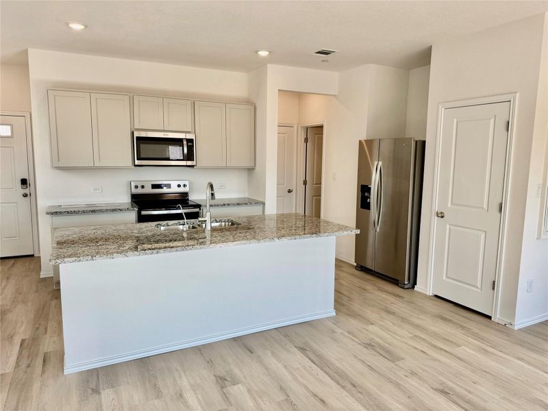 Kitchen featuring appliances with stainless steel finishes, light wood-type flooring, a kitchen island with sink, light stone countertops, and recessed lighting Kitchen featuring appliances with stainless steel finishes, light wood-type flooring, a kitchen island with sink, light stone countertops, and recessed lighting
