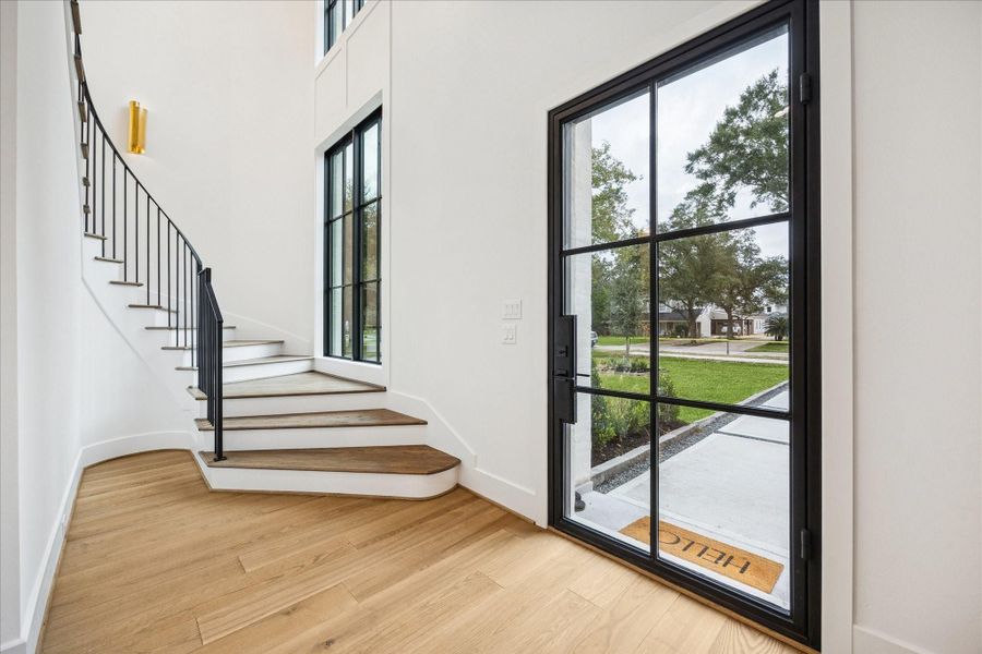 Floor-to-ceiling Pella Reserve windows illuminate the curved staircase and wide-plank oak floors, creating an open, welcoming entry with elegant vertical volume. Soaring ceiling heights carried throughout the home set this build apart from typical new construction.