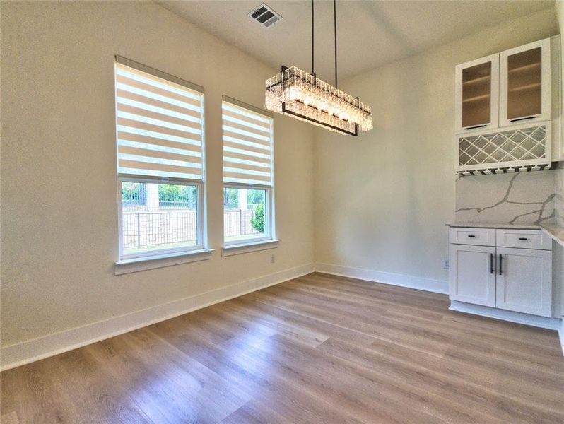 Dining area featuring wood-finish flooring, two large windows with blinds, and a built-in beverage bar