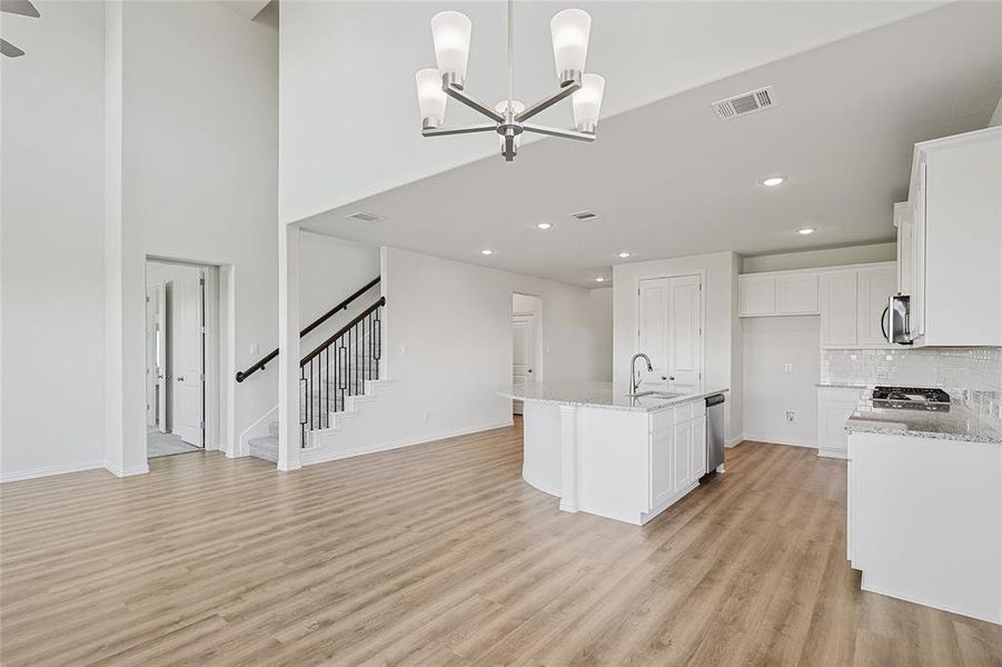 Kitchen with white cabinetry, stainless steel appliances, light hardwood / wood-style flooring, and a center island with sink