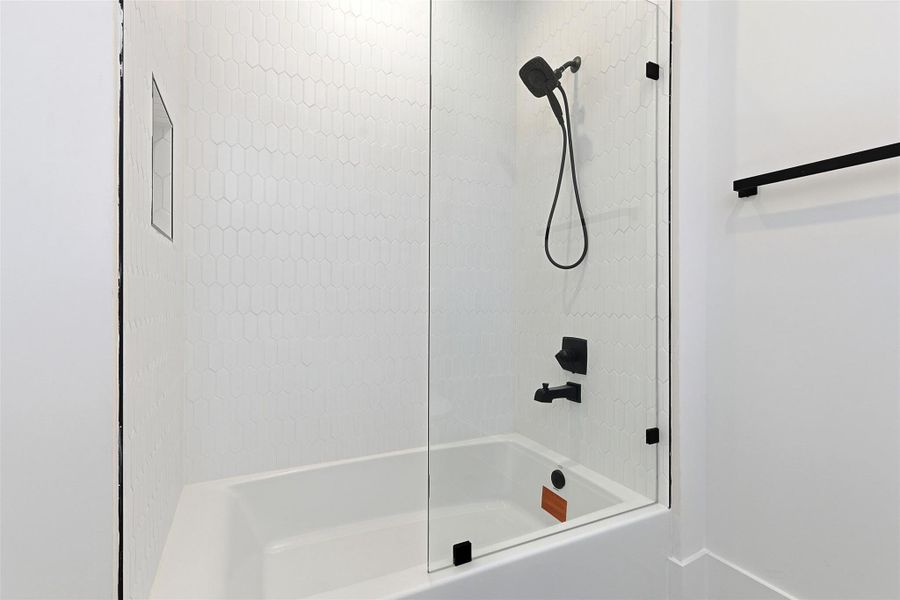 A soaking tub is paired with a glass partition and features a white hexagonal tile backsplash.