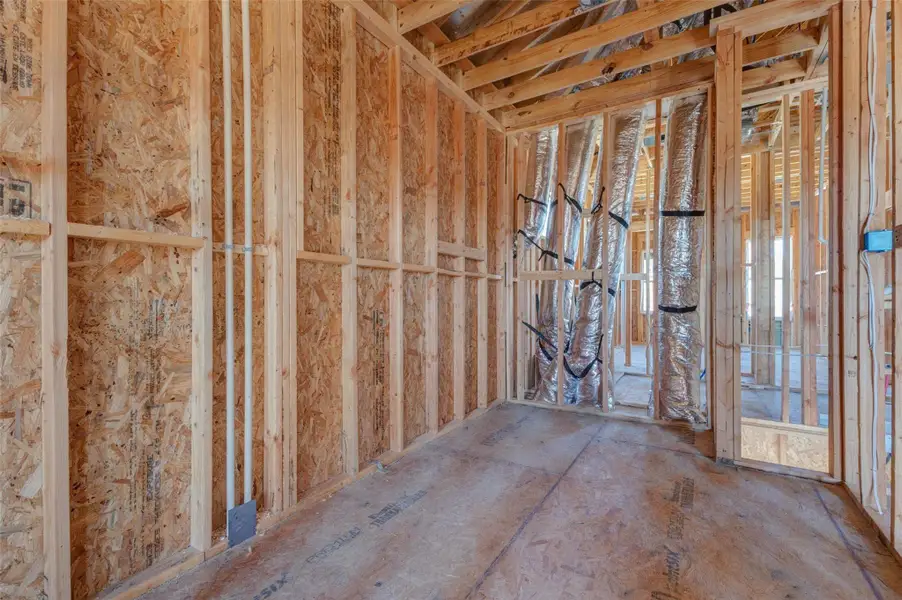 Framed interior room with exposed wood structure, OSB sheathing, and visible HVAC ductwork running through the wall openings. This construction-stage photo offers a close behind-the-scenes look at the build quality, room proportions, and future finished layout as the home continues moving toward completion. Framed interior room with exposed wood structure, OSB sheathing, and visible HVAC ductwork running through the wall openings. This construction-stage photo offers a close behind-the-scenes look at the build quality, room proportions, and future finished layout as the home continues moving toward completion.