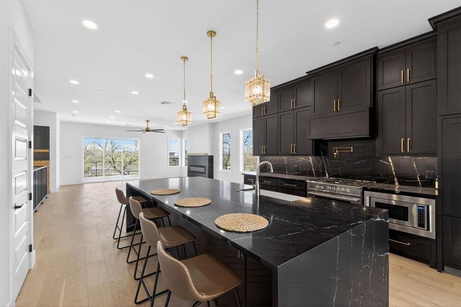 Kitchen featuring dark stone countertops, a fireplace, a breakfast bar area, light wood-style flooring, and stainless steel appliances