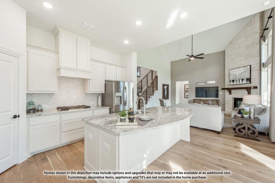 Open-concept kitchen with white cabinets, granite island, and living room with stone fireplace visible beyond