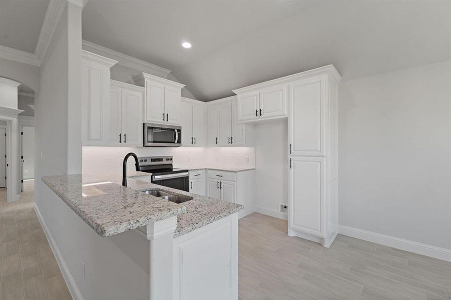 Kitchen featuring white cabinets, stainless steel appliances, light wood-style floors, vaulted ceiling, and ornamental molding