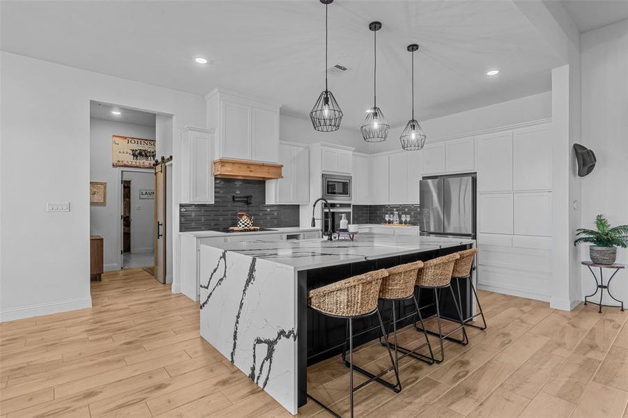 Kitchen featuring white cabinets, a spacious island, stainless steel appliances, and light hardwood / wood-style flooring