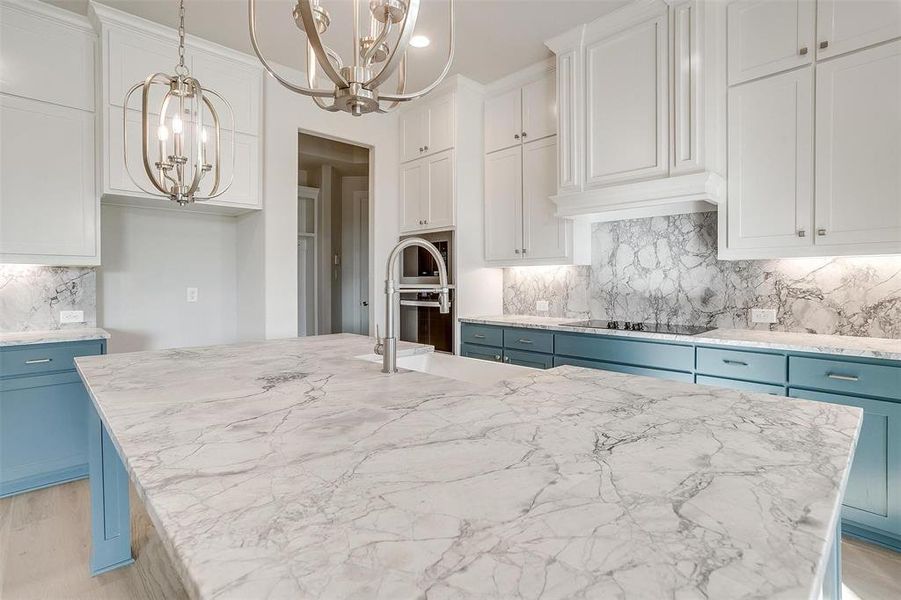 Kitchen featuring a kitchen island with sink, black electric stovetop, white cabinets, and decorative light fixtures