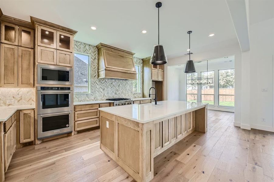 Kitchen with backsplash, custom exhaust hood, an island with sink, and light hardwood / wood-style floors