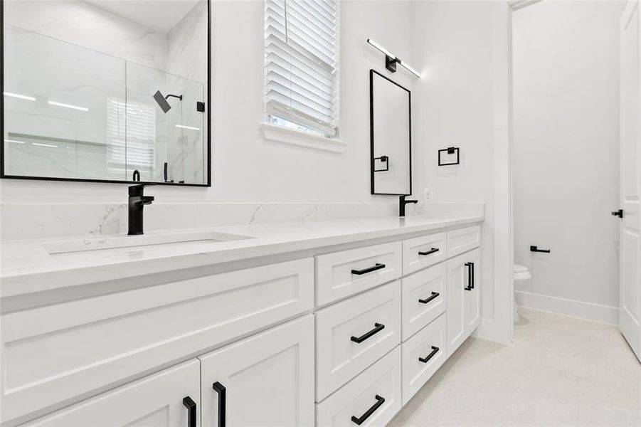 Dual vanity featuring white shaker-style cabinetry with matte black hardware, integrated sinks, and light-toned countertops