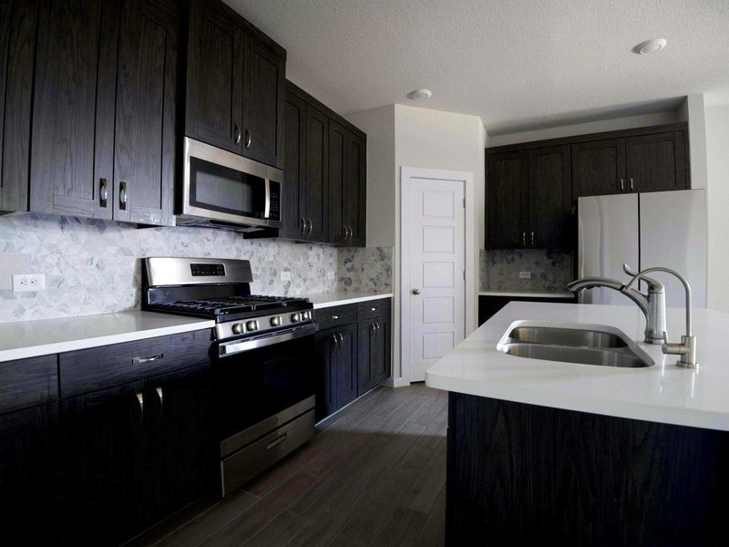 Kitchen featuring stainless steel appliances, backsplash, dark wood-style flooring, a textured ceiling, and light stone counters Kitchen featuring stainless steel appliances, backsplash, dark wood-style flooring, a textured ceiling, and light stone counters