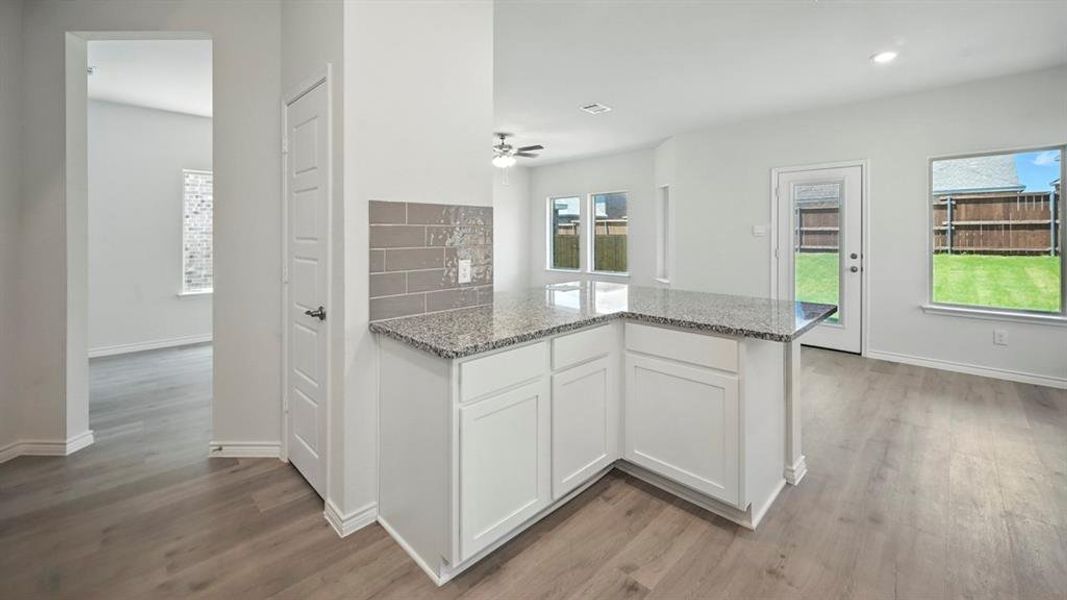 Kitchen featuring a peninsula, white cabinets, light stone countertops, light wood-style floors, and a ceiling fan