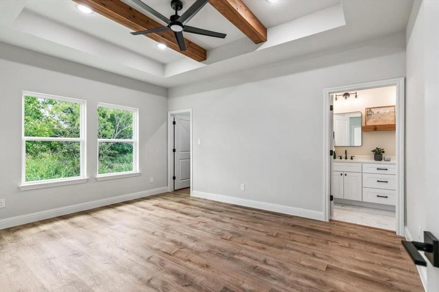 Spacious room featuring wood-finish flooring, a tray ceiling with exposed wooden beams, and a black ceiling fan