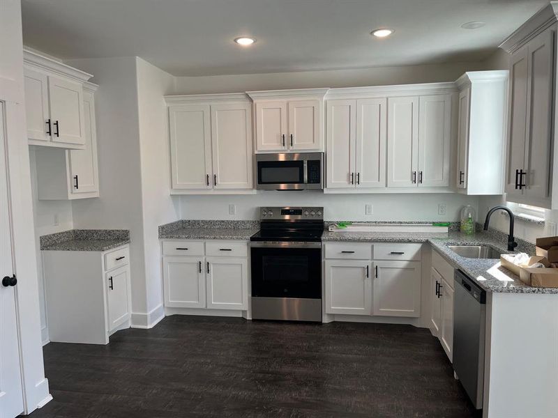 Kitchen with stainless steel appliances, white cabinets, light stone counters, dark wood-type flooring, and recessed lighting