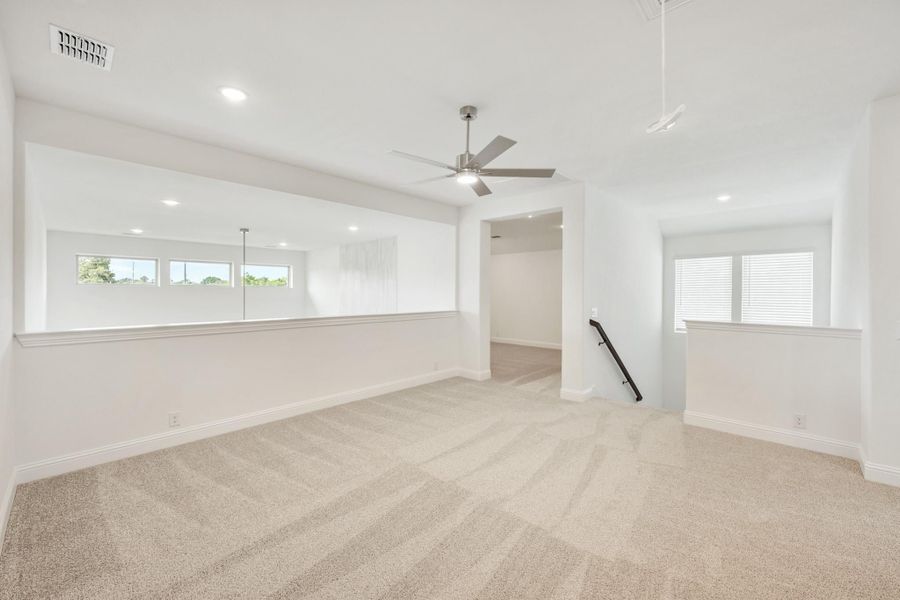 Spacious bonus room with beige carpet, ceiling fan, white walls, and staircase landing nearby