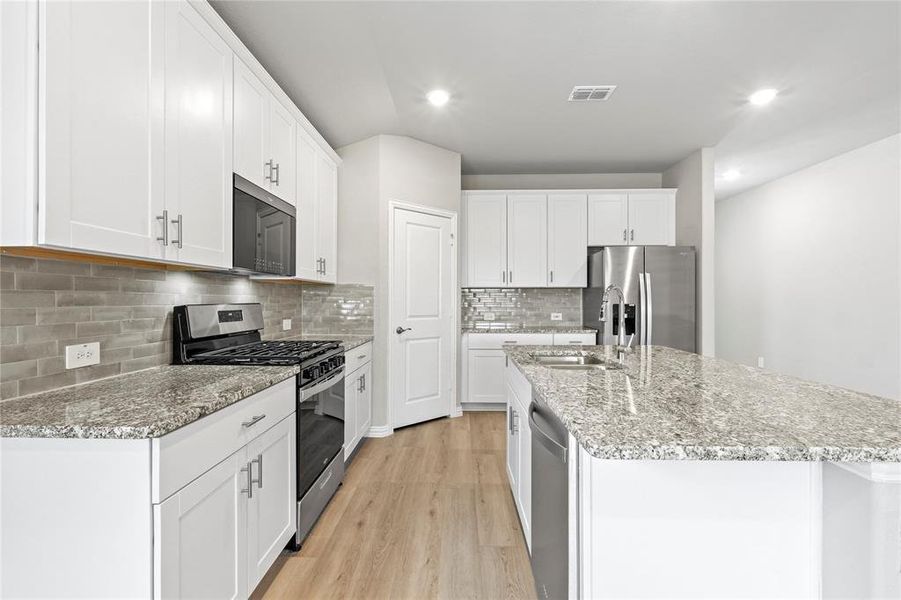 Kitchen featuring appliances with stainless steel finishes, light wood finished floors, a kitchen island with sink, white cabinets, and recessed lighting Kitchen featuring appliances with stainless steel finishes, light wood finished floors, a kitchen island with sink, white cabinets, and recessed lighting