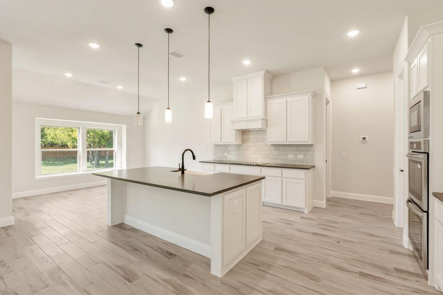 Kitchen with white cabinets, dark countertop island, pendant lights, and light wood floors