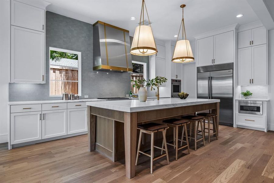 Kitchen with backsplash, wall chimney exhaust hood, light hardwood / wood-style flooring, and built in appliances