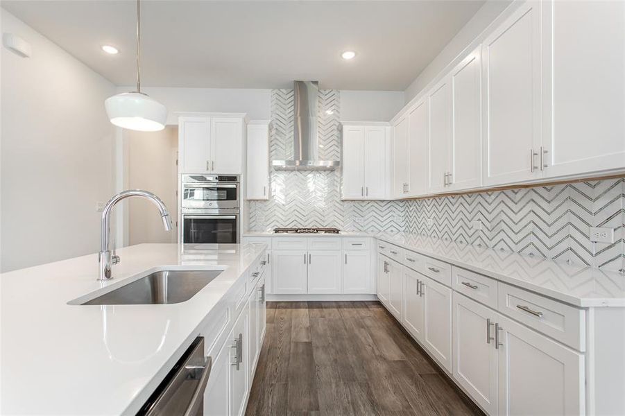 Kitchen featuring pendant lighting, sink, wall chimney exhaust hood, white cabinetry, and stainless steel appliances