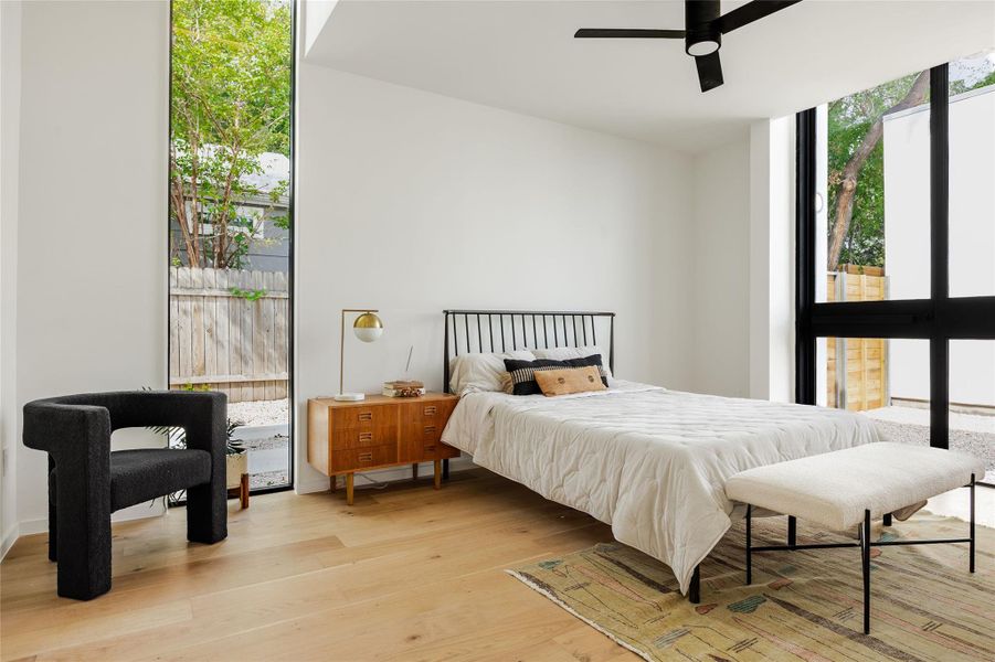 Bedroom featuring wood finished floors, expansive windows, and ceiling fan